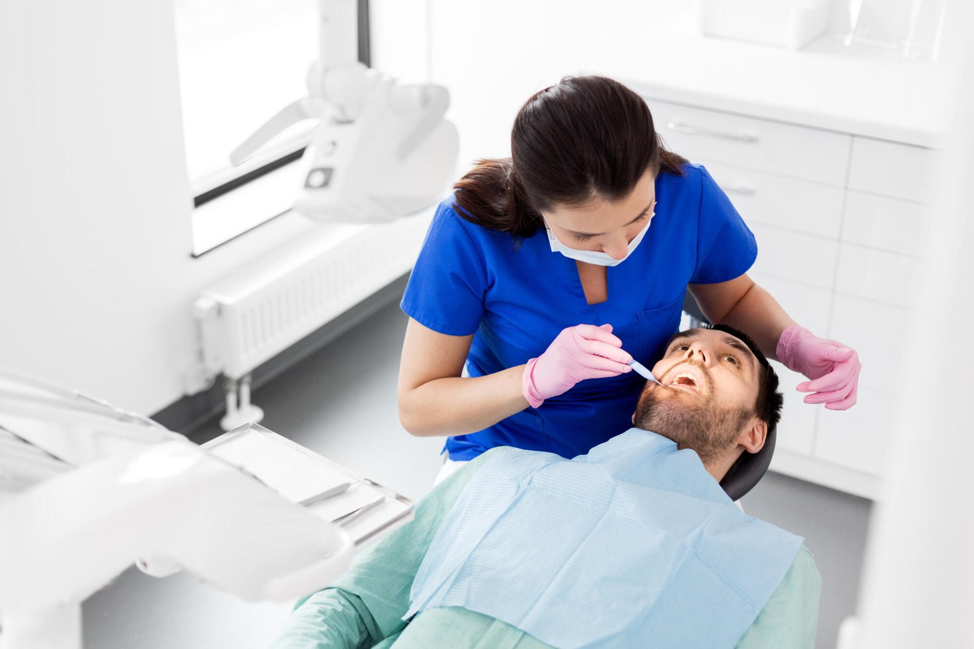 Dentist examining a patient's teeth. Dental office, woman in blue scrubs, man in chair.