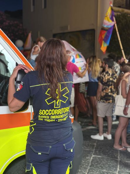 Un membro dell'equipaggio di un'ambulanza a un evento del Pride. Persone con bandiere, vicino al veicolo.