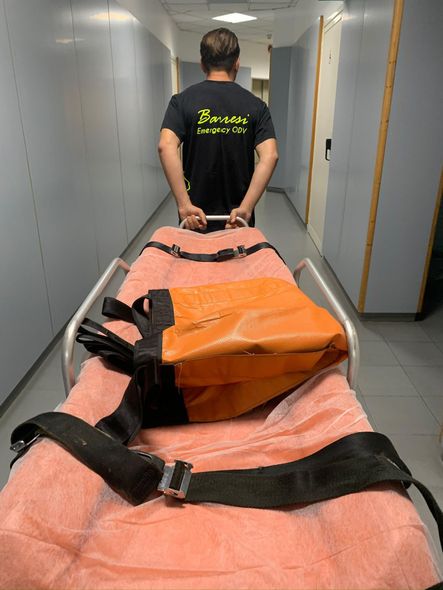 Persona che trascina una barella lungo un corridoio. Sulla barella è appoggiata una borsa.