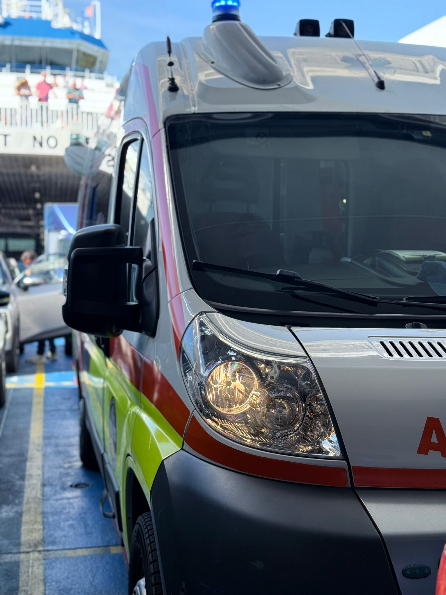 Ambulanza su un traghetto, con luci blu lampeggianti e strisce rosse e gialle.