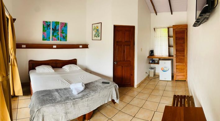 Habitación pequeña con cama, suelo de baldosas, puertas de madera y una cocina pequeña en la parte trasera.