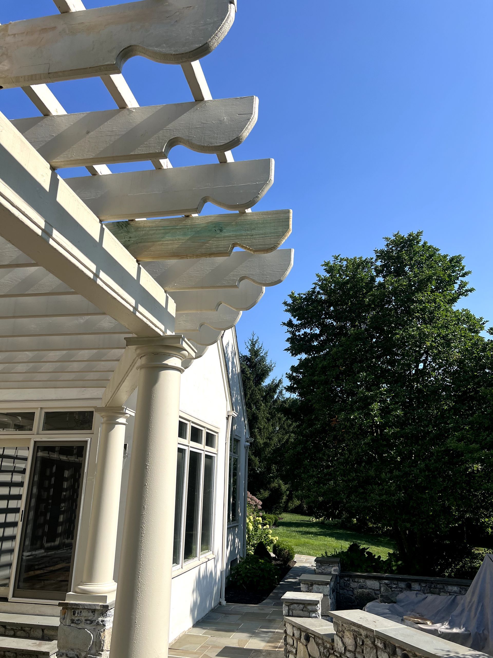 White pergola with blue sky, a building, and a green tree in the background.