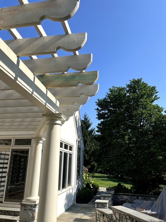 White pergola with blue sky, a building, and a green tree in the background.