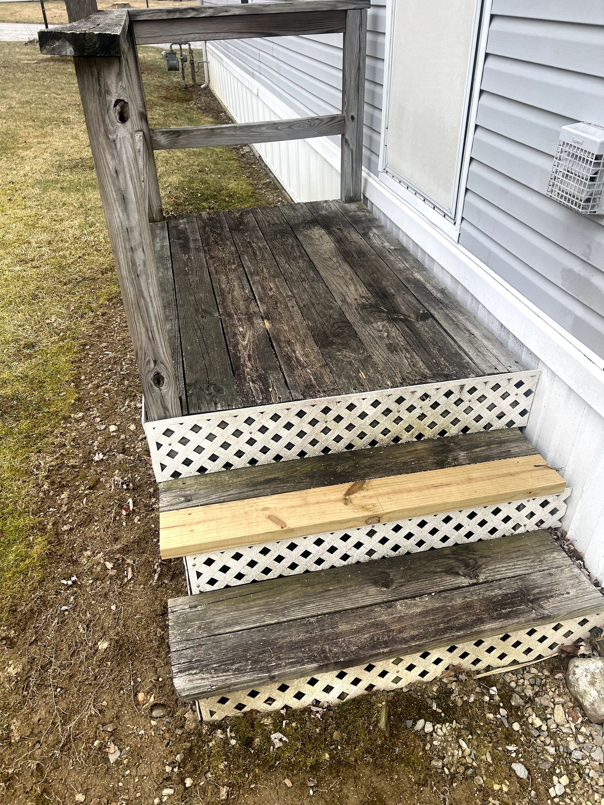 Wooden porch and steps; weathered and discolored, lattice trim.