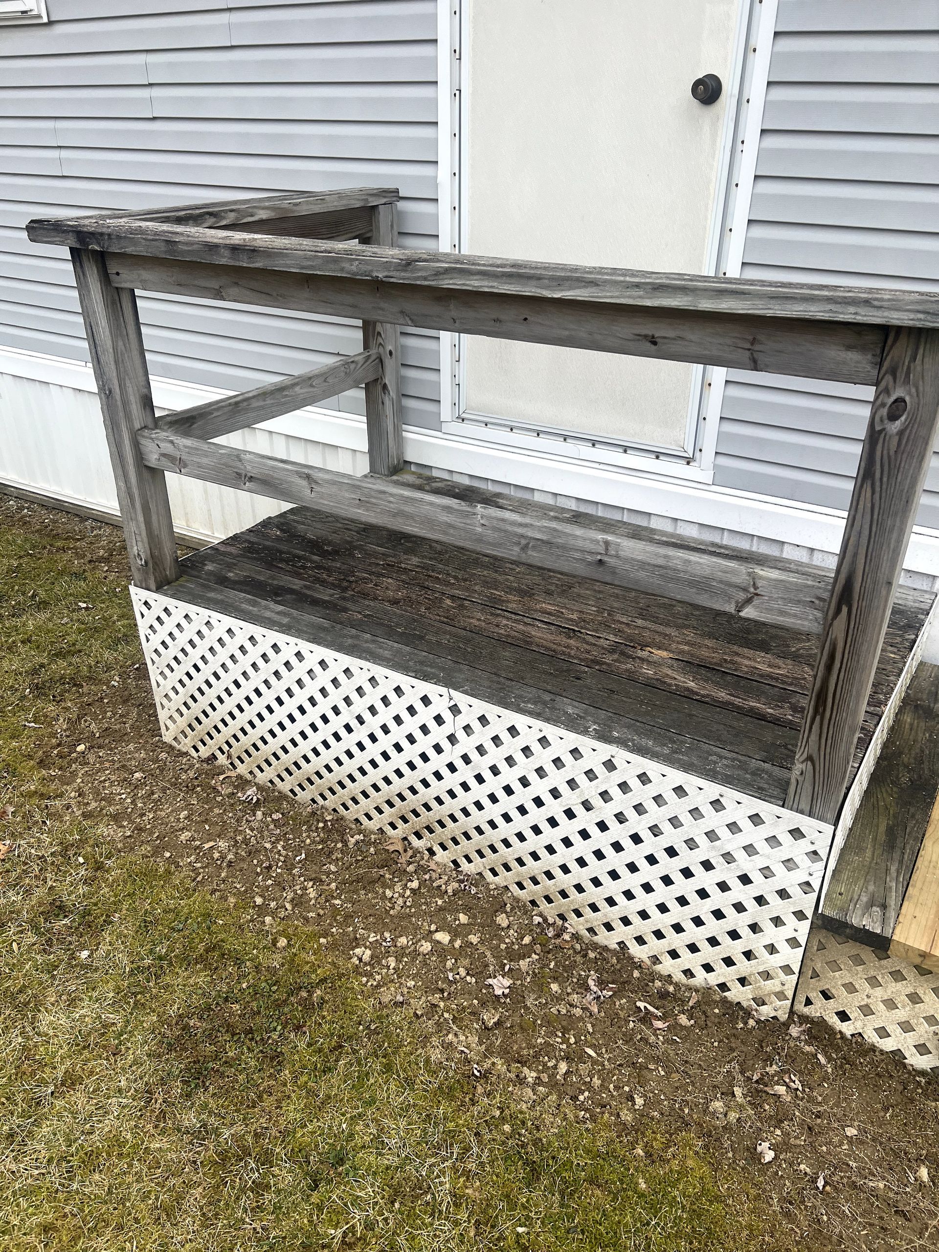 Wooden porch with railing, attached to a gray siding house, and white lattice skirting.