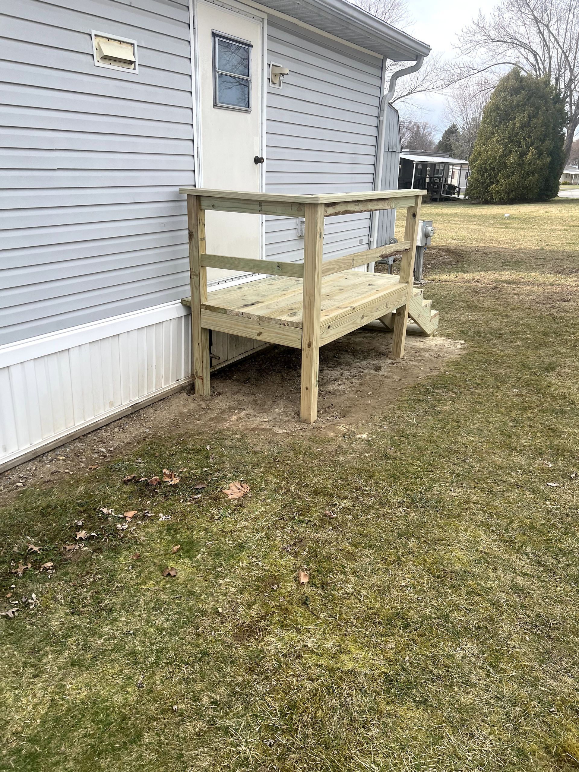 A small wooden deck with a railing outside a light blue house.