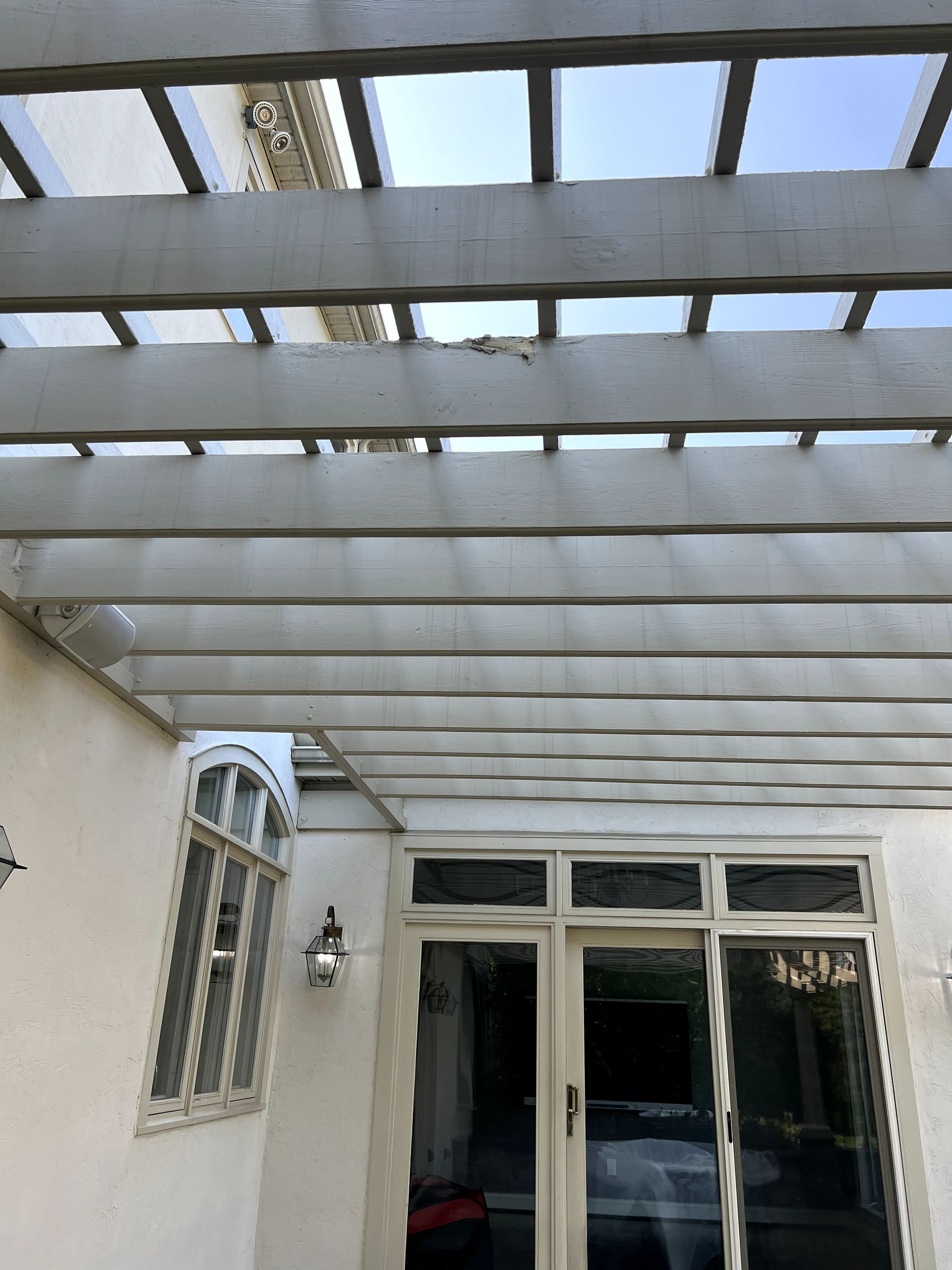 A white pergola over a patio with a window and sliding glass doors.