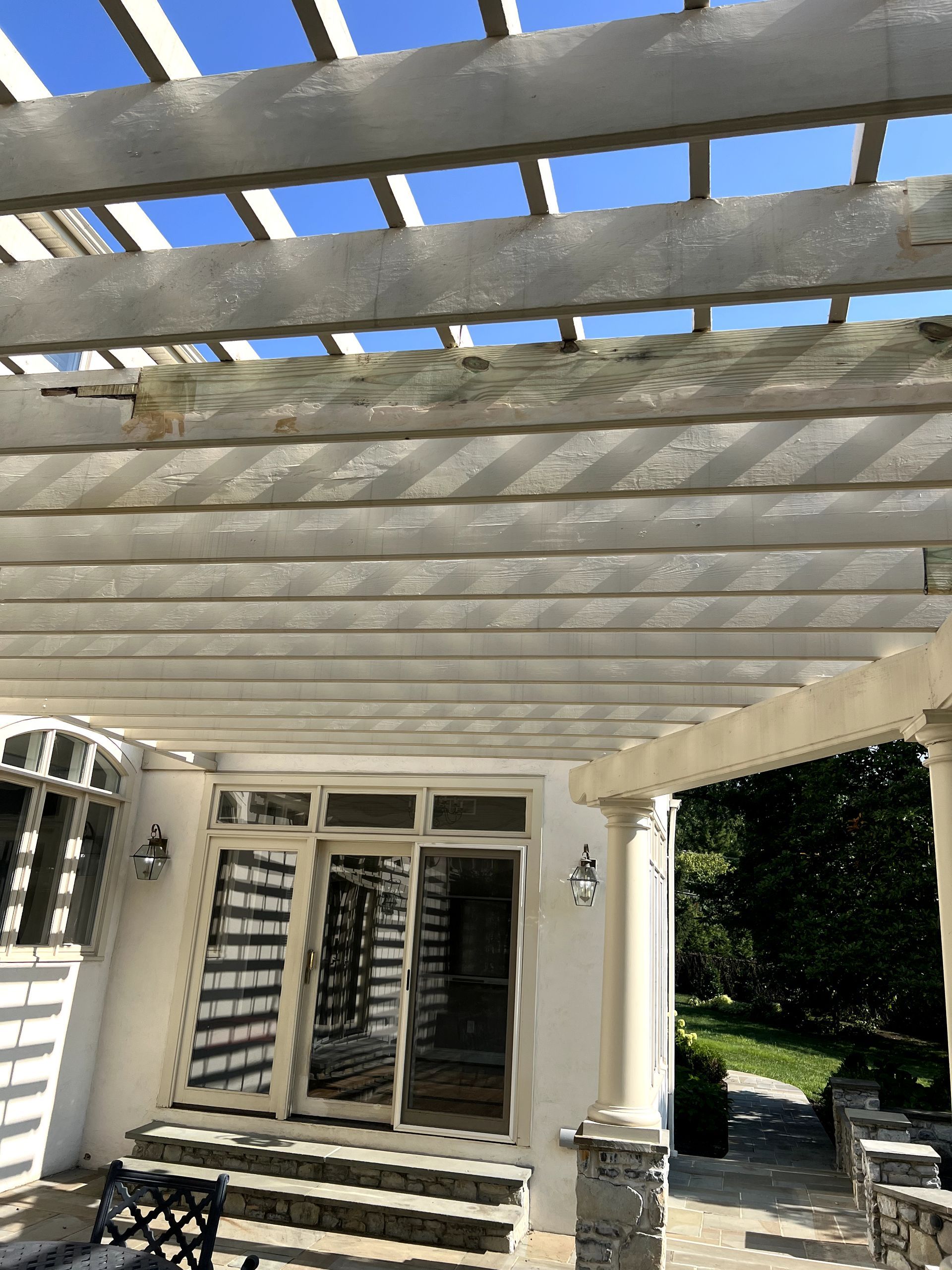 Pergola over white patio and house entrance with clear sky.