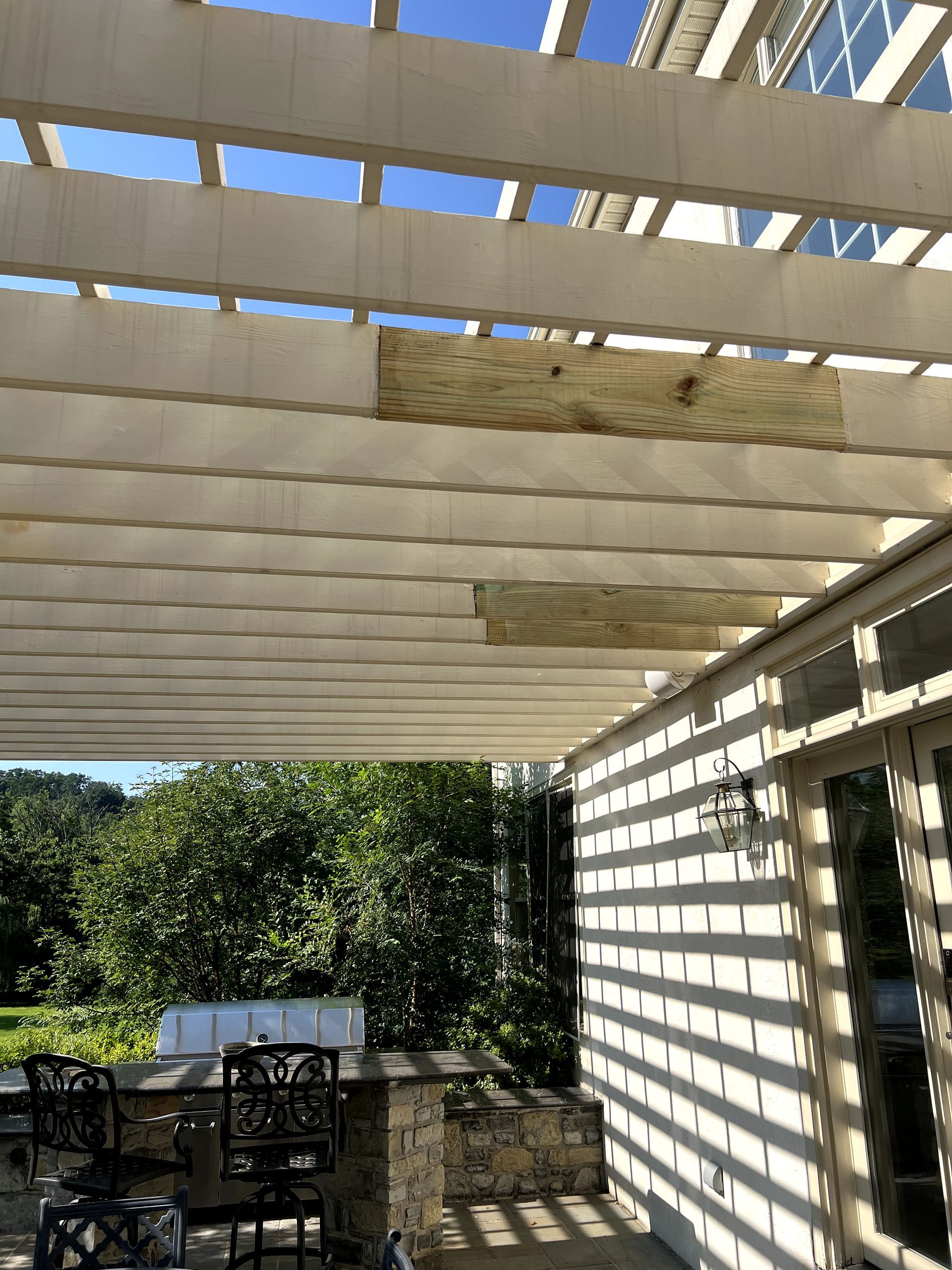 White pergola with light shining on a beige wall, stone terrace below.