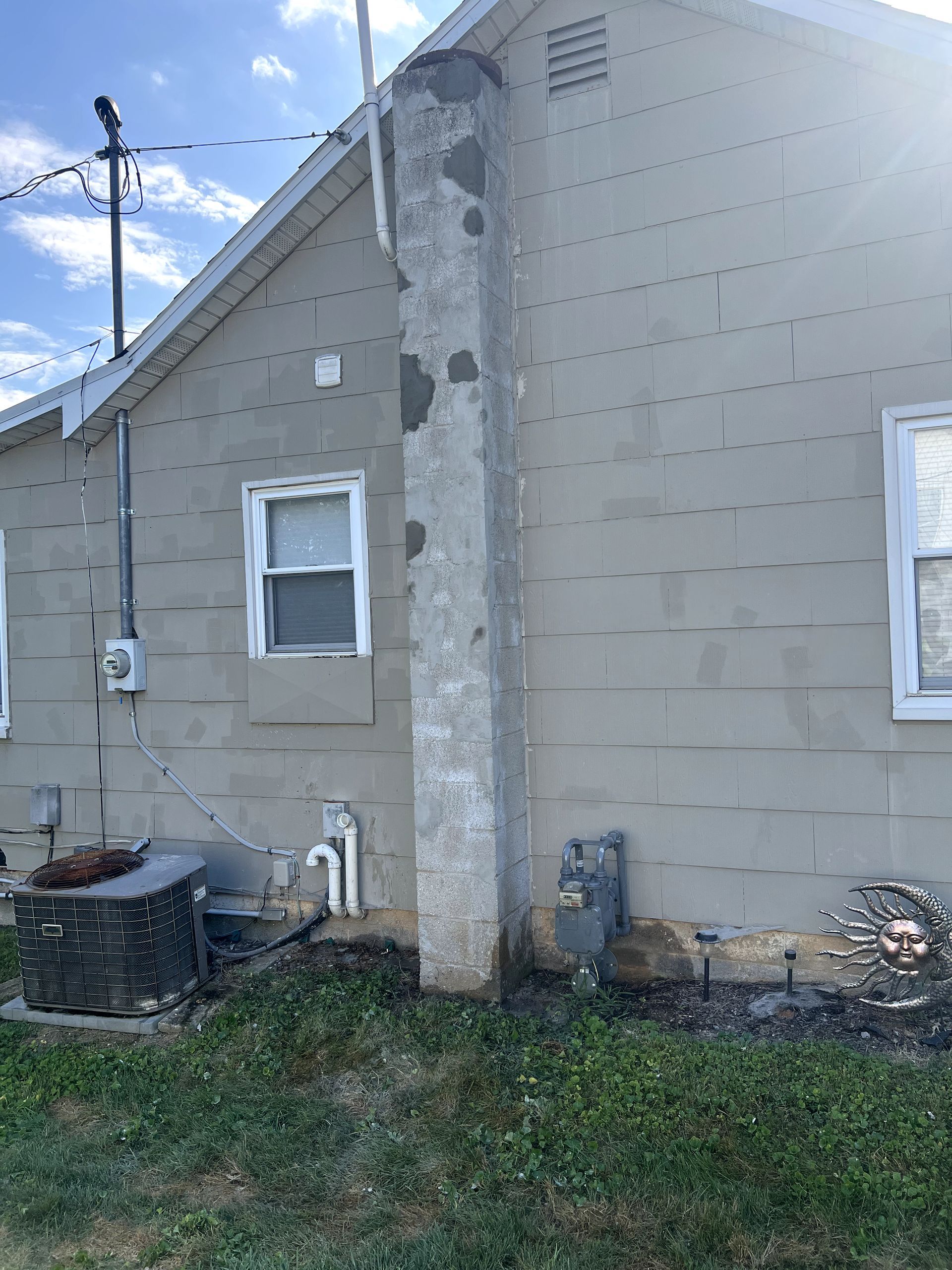 Side view of a house with a gray chimney, windows, and gas meter.