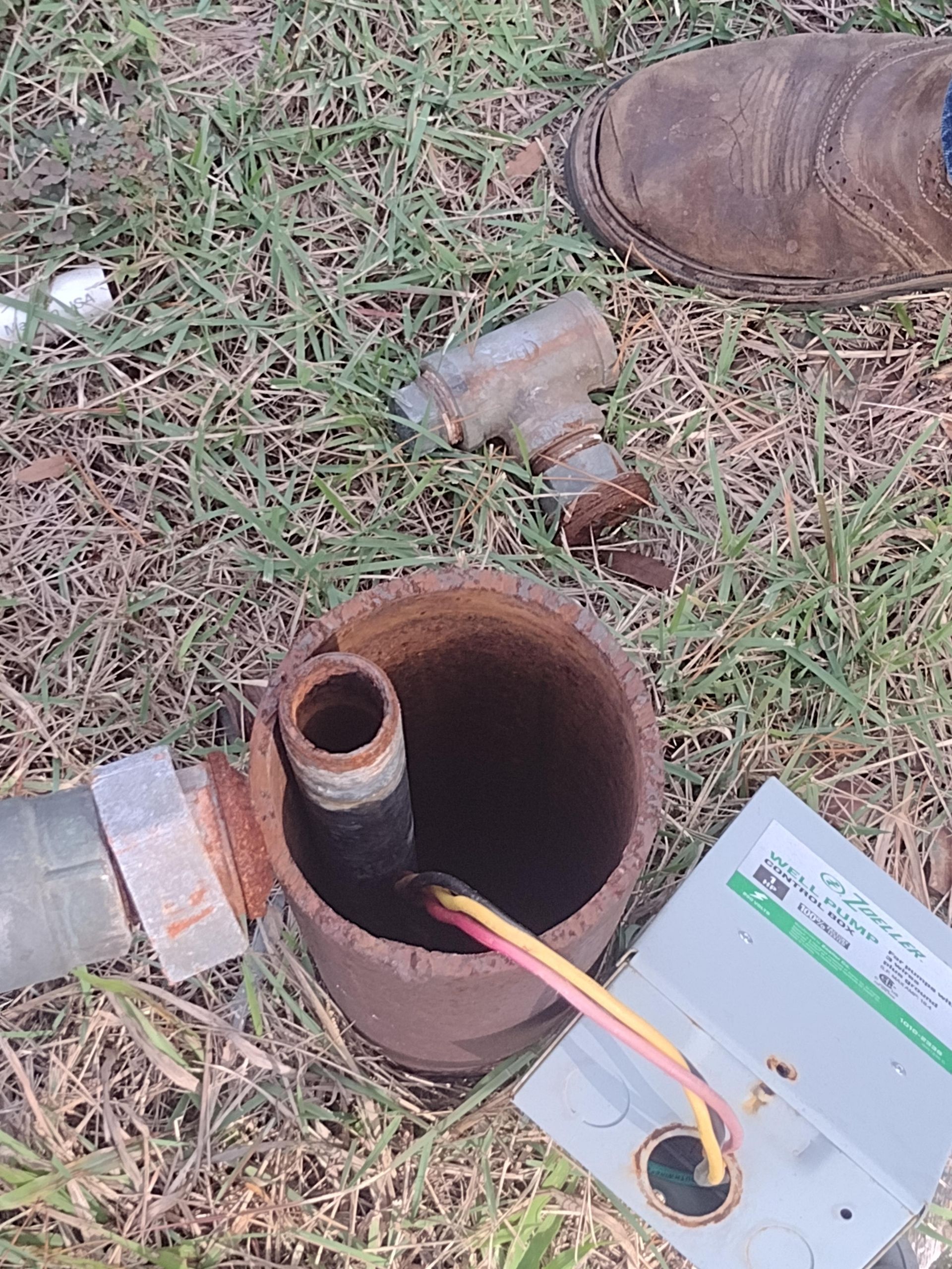 Rusty well components with electrical wire on grass.