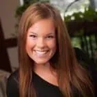 A woman with long brown hair is smiling and wearing a black shirt.