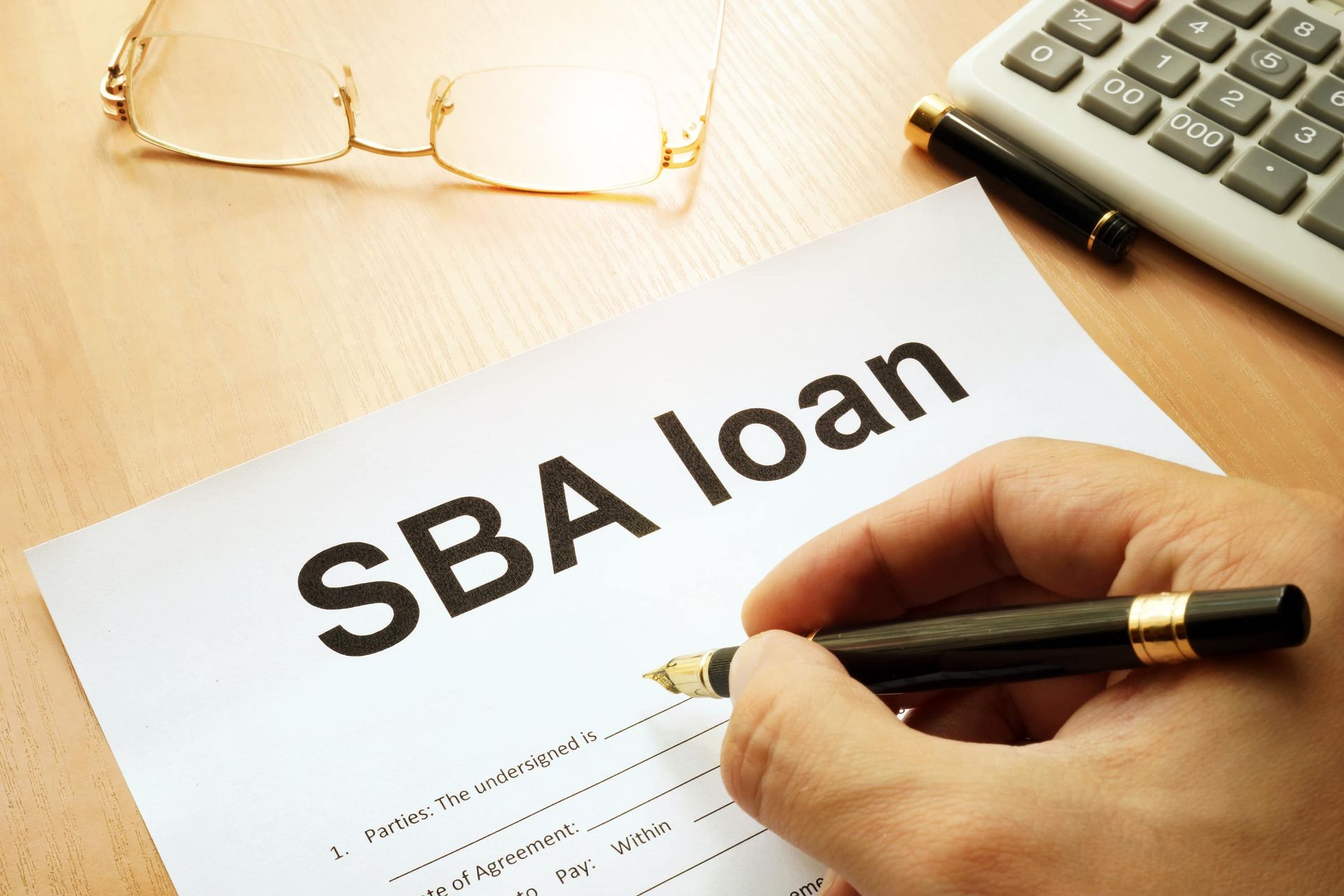 Hand writing on an SBA loan form beside glasses and a calculator