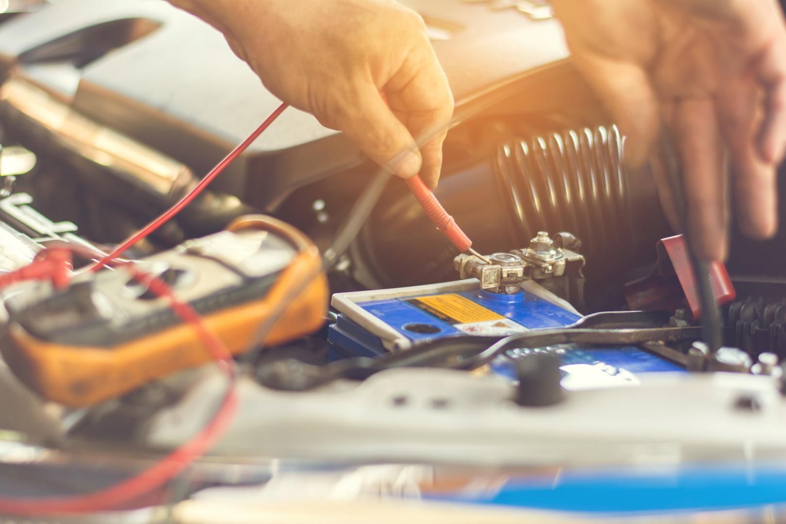 Un mécanicien utilise un multimètre pour tester une batterie de voiture dans un compartiment moteur.