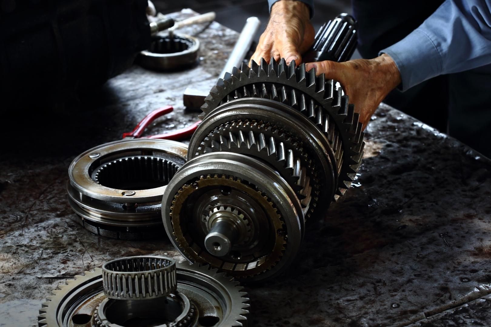 Mains d'un mécanicien tenant des engrenages. Plusieurs engrenages de tailles variées et pièces métalliques sur une surface graisseuse.