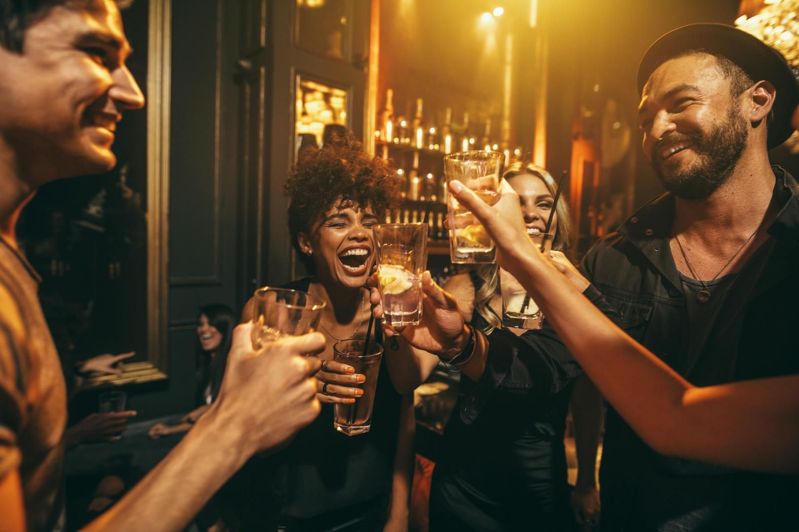 A group of people are toasting with drinks in a bar.