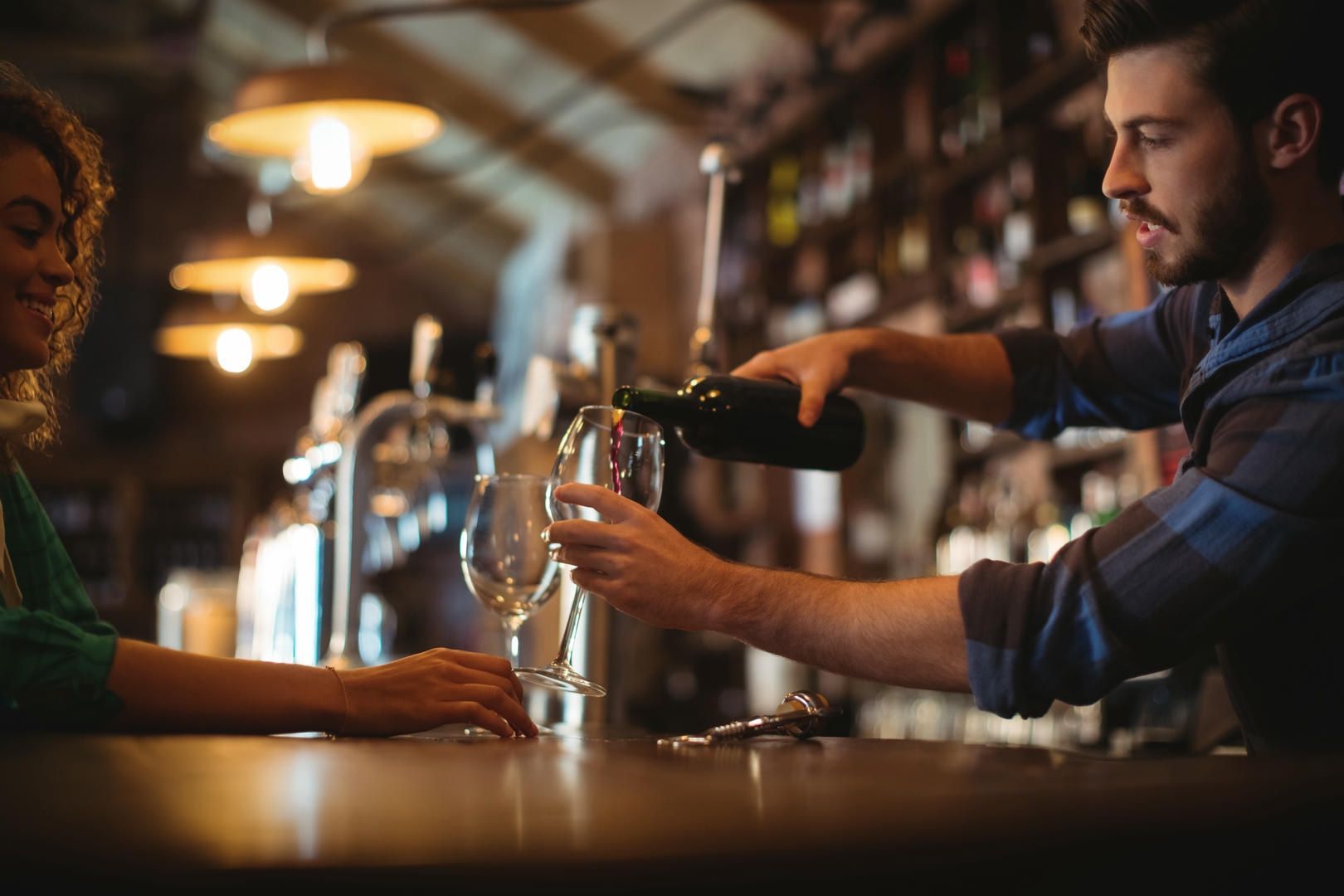 A man is pouring wine into a glass for a woman at a bar.