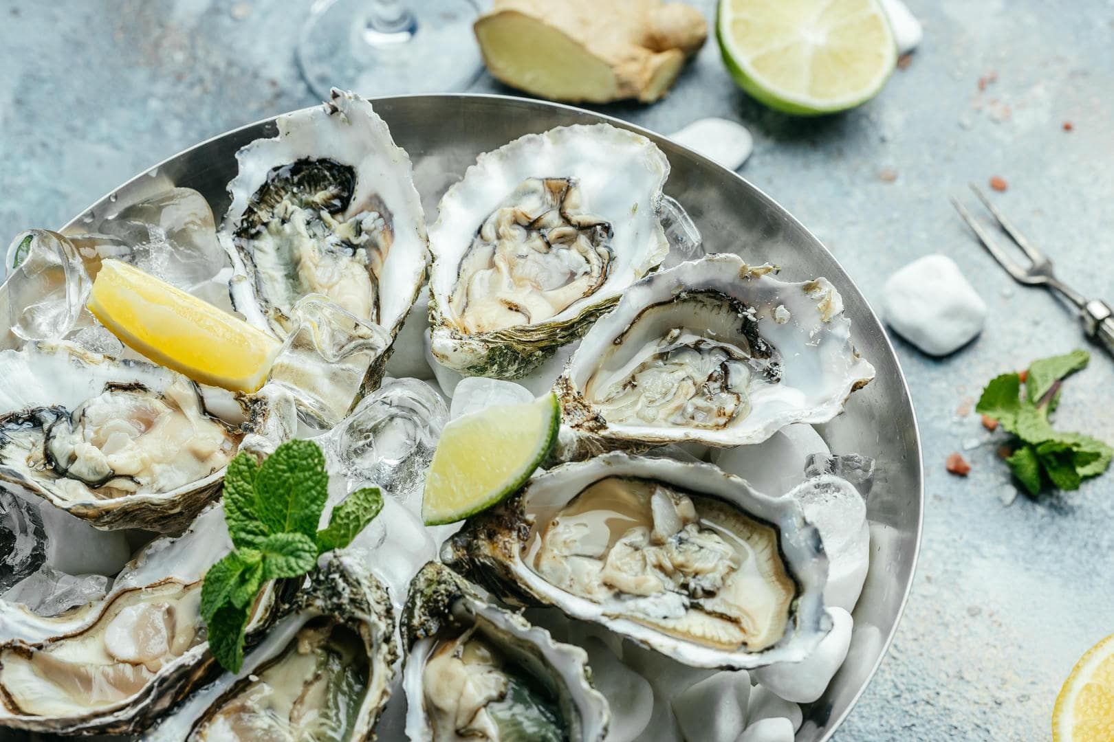 A plate of oysters with lemon and mint on ice.