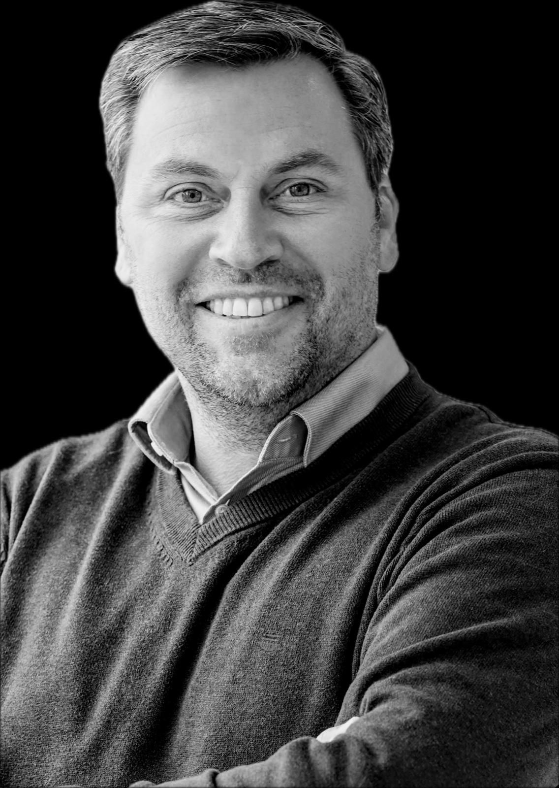 Lachende man, gekleed in een donkere trui en een overhemd met kraag. Zwarte achtergrond.