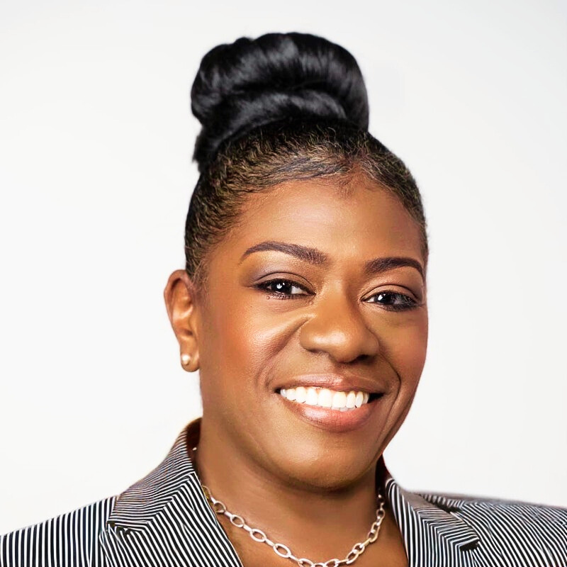 A woman is sitting at a desk with a laptop and a vase of flowers.