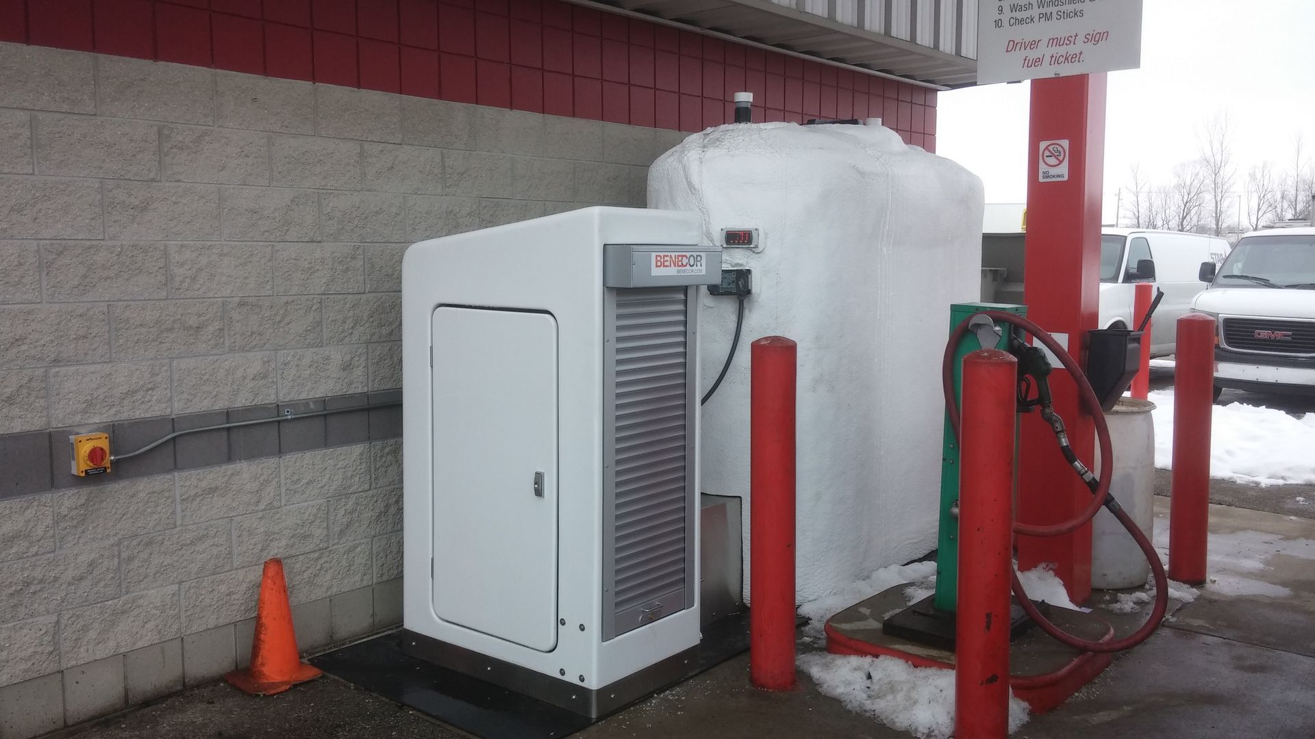 White fueling station equipment outside a building with red accents, covered in snow.