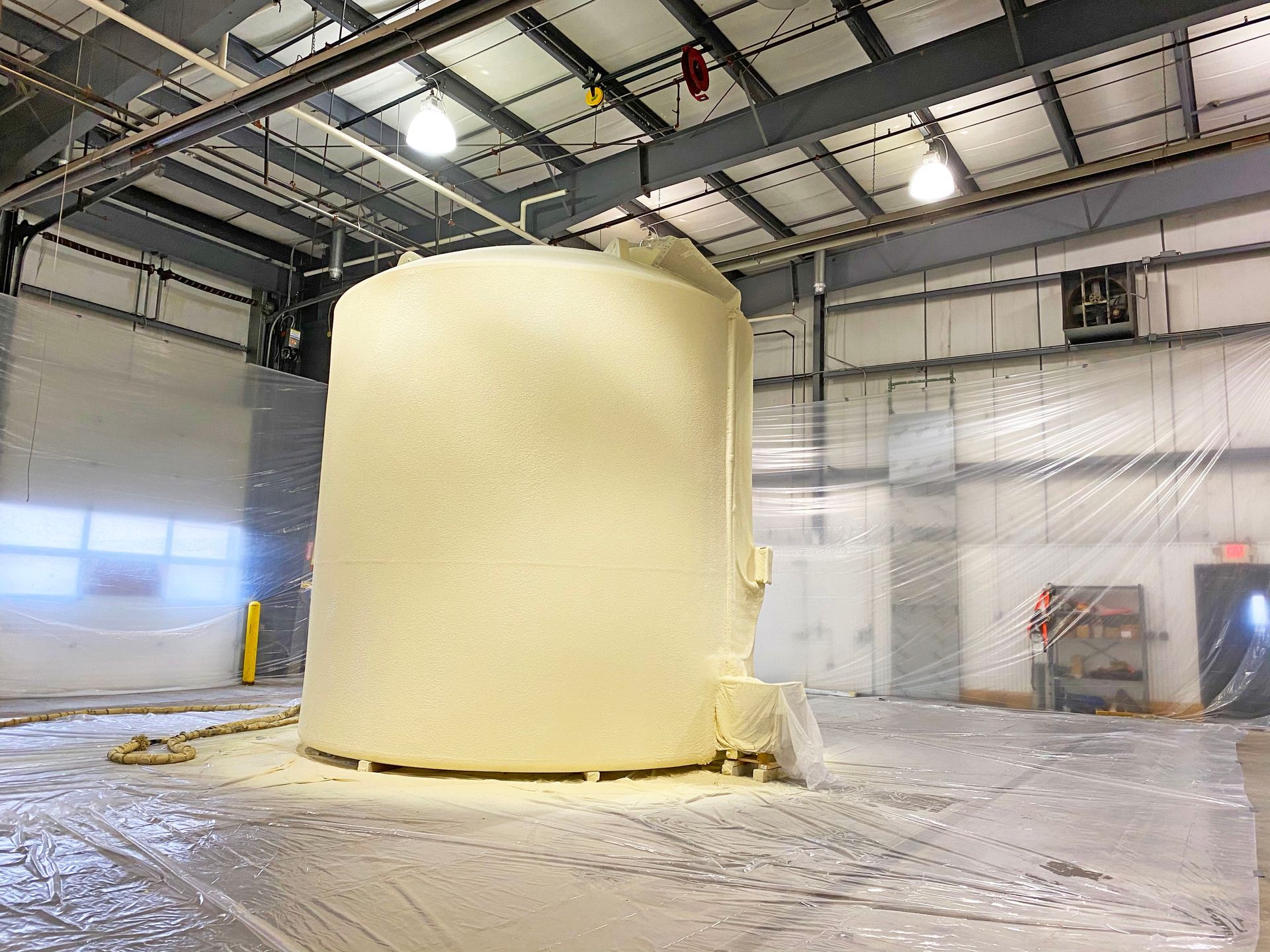 Large cylindrical object covered in foam inside a warehouse, wrapped in plastic sheeting.