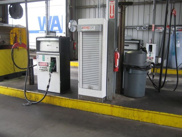 Fuel pump and ventilation unit inside a service bay, next to a trash can and fire extinguisher.