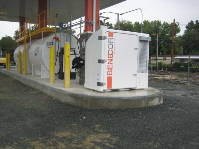 Gas station with a white tank, fuel pumps, and a BENECOR branded cabinet.