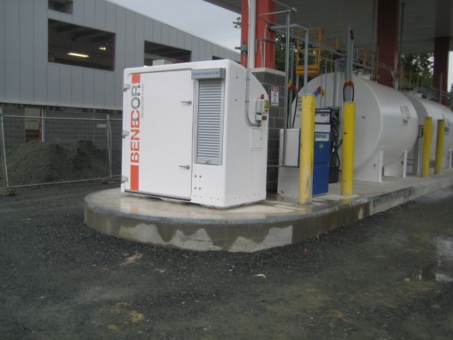 A white and red Generac generator beside a large fuel tank at a gas station.
