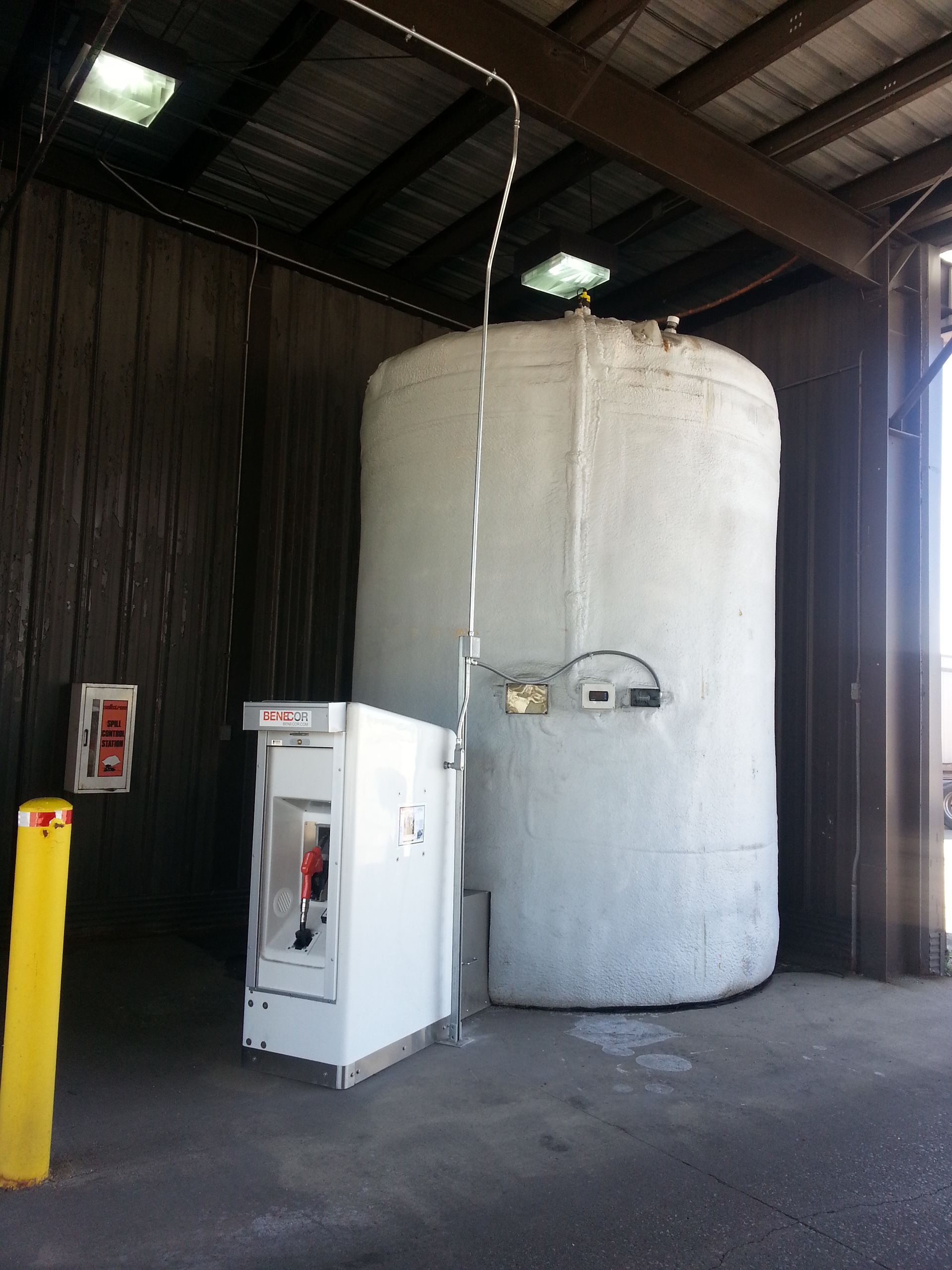 White industrial tank with attached dispenser in a shed, safety devices visible.