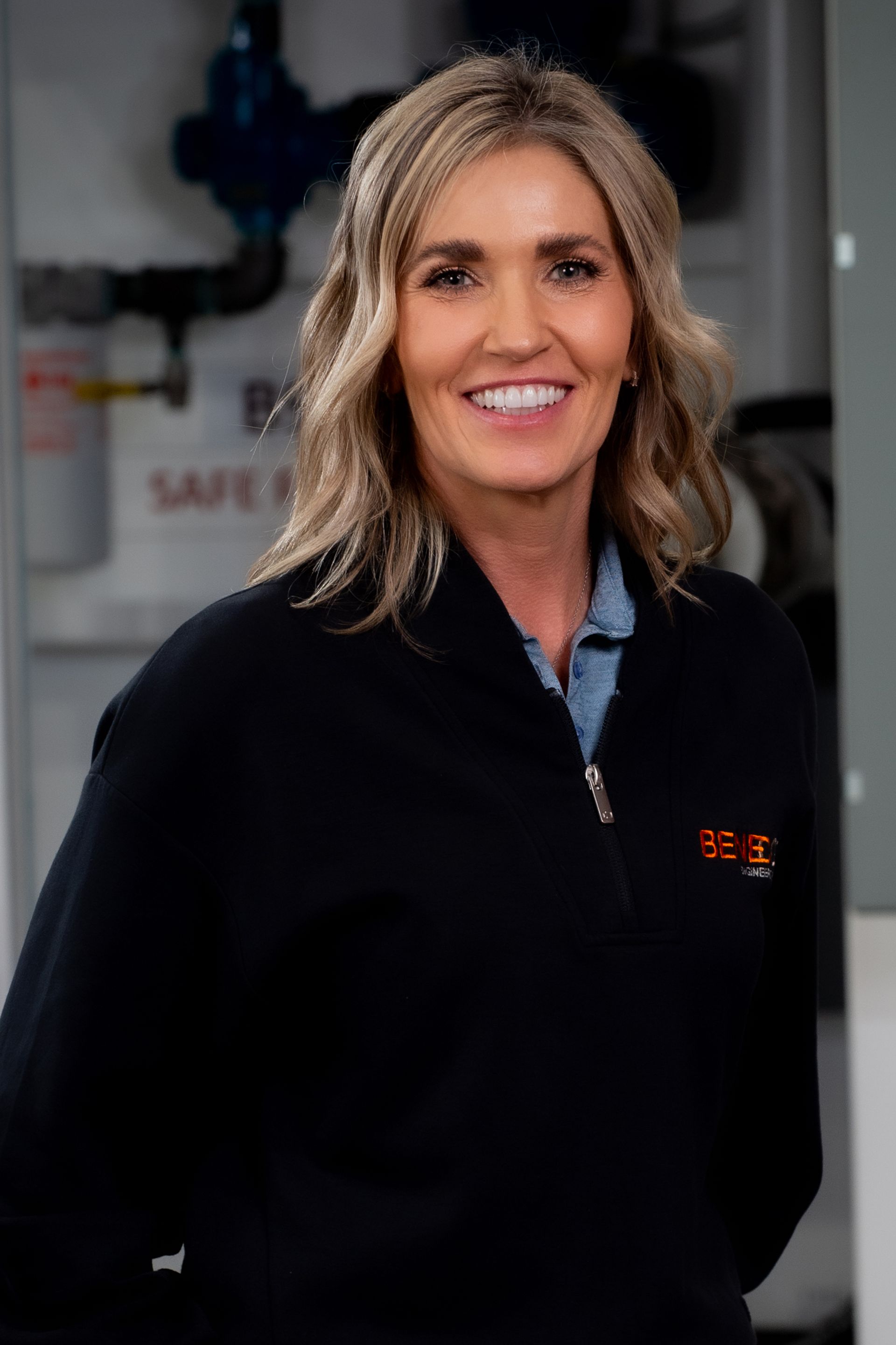 Woman in black jacket, smiling in front of equipment.