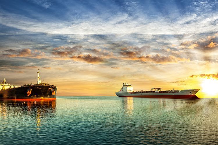 Two cargo ships on the ocean at sunset, with orange and yellow sky and sun rays.