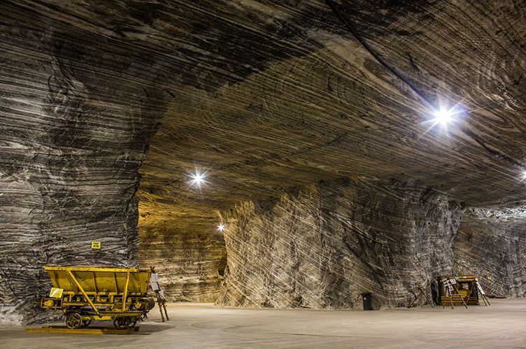 Large salt mine interior, showing cavernous space, yellow mine cart, and workers.