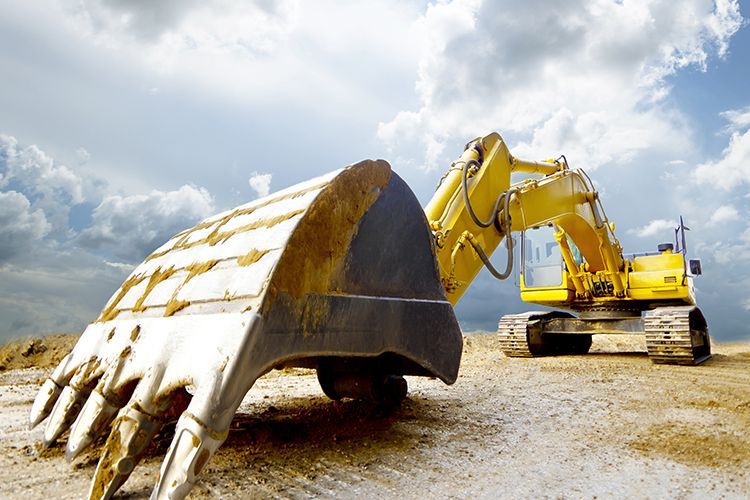 Yellow excavator on a construction site, under a cloudy sky. The bucket is in the foreground.
