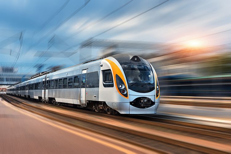 High-speed train speeding along tracks, silver and yellow design, motion blur, outdoor setting.