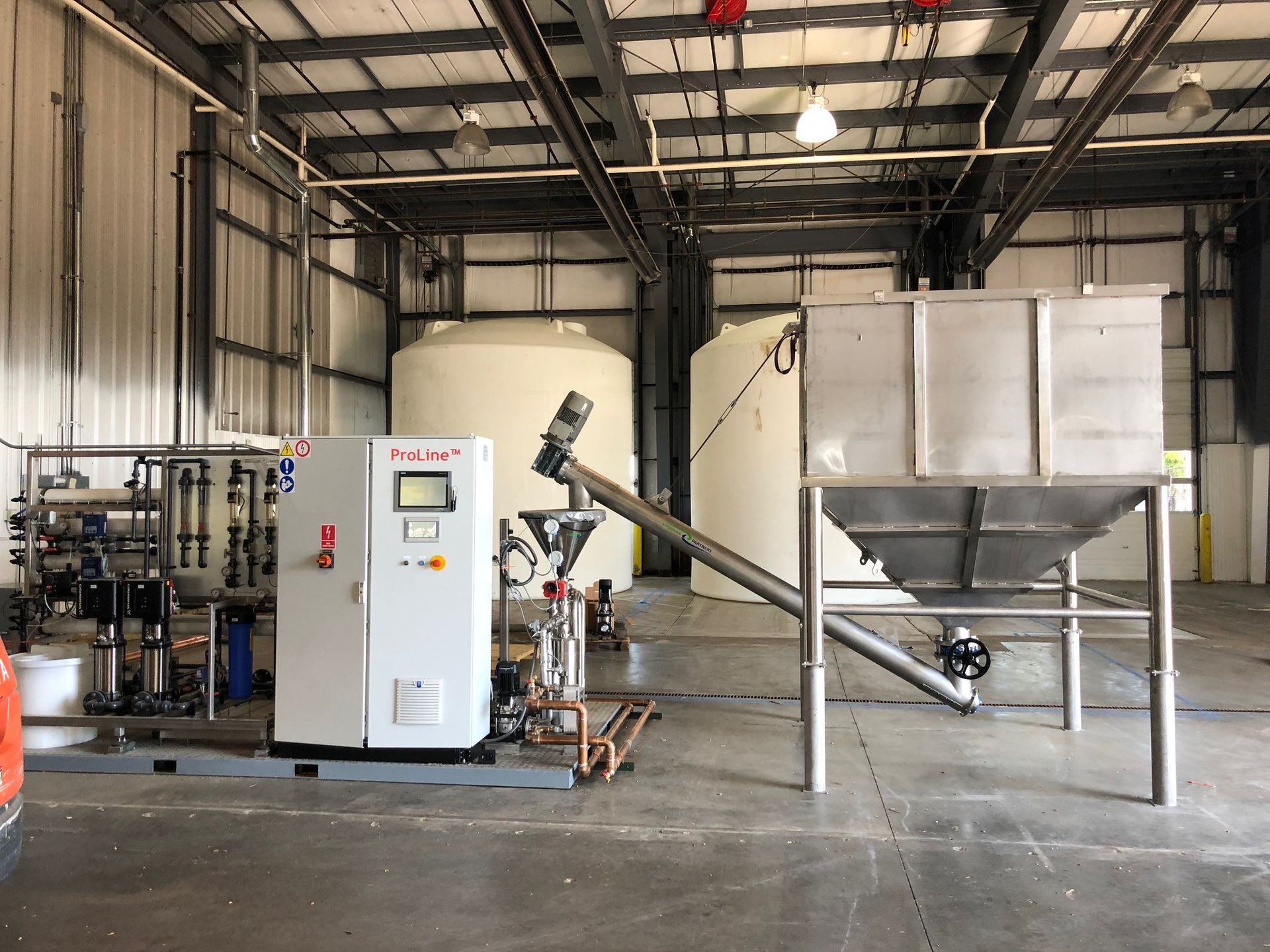 Industrial facility interior with tanks, machinery, and a control panel, likely for chemical processing.