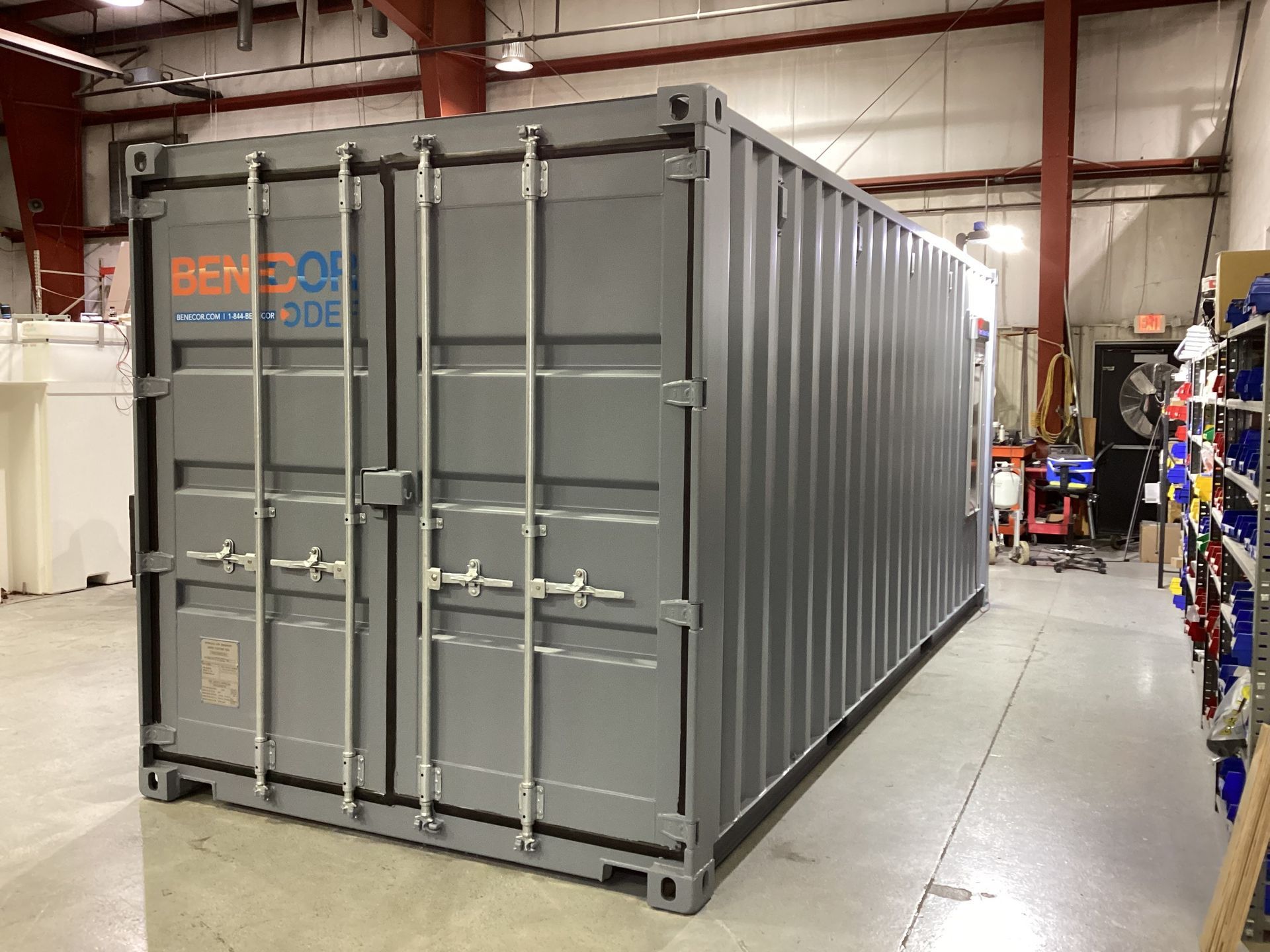 Gray shipping container inside a building, next to shelving.