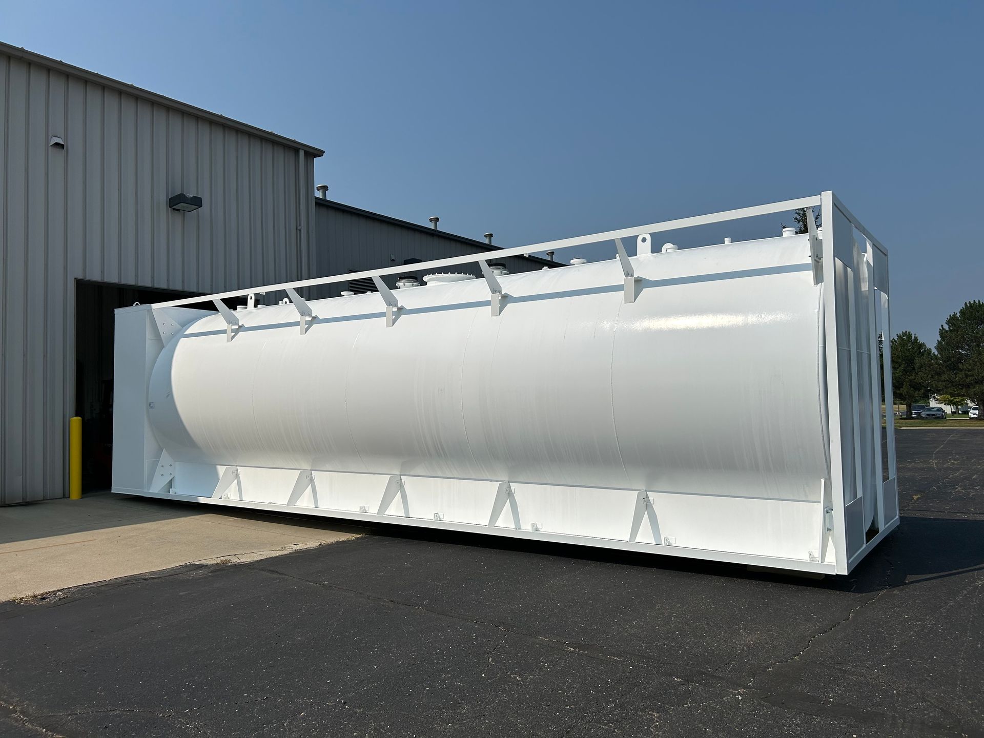 White industrial tank outside a building, on a paved surface, in sunlight.