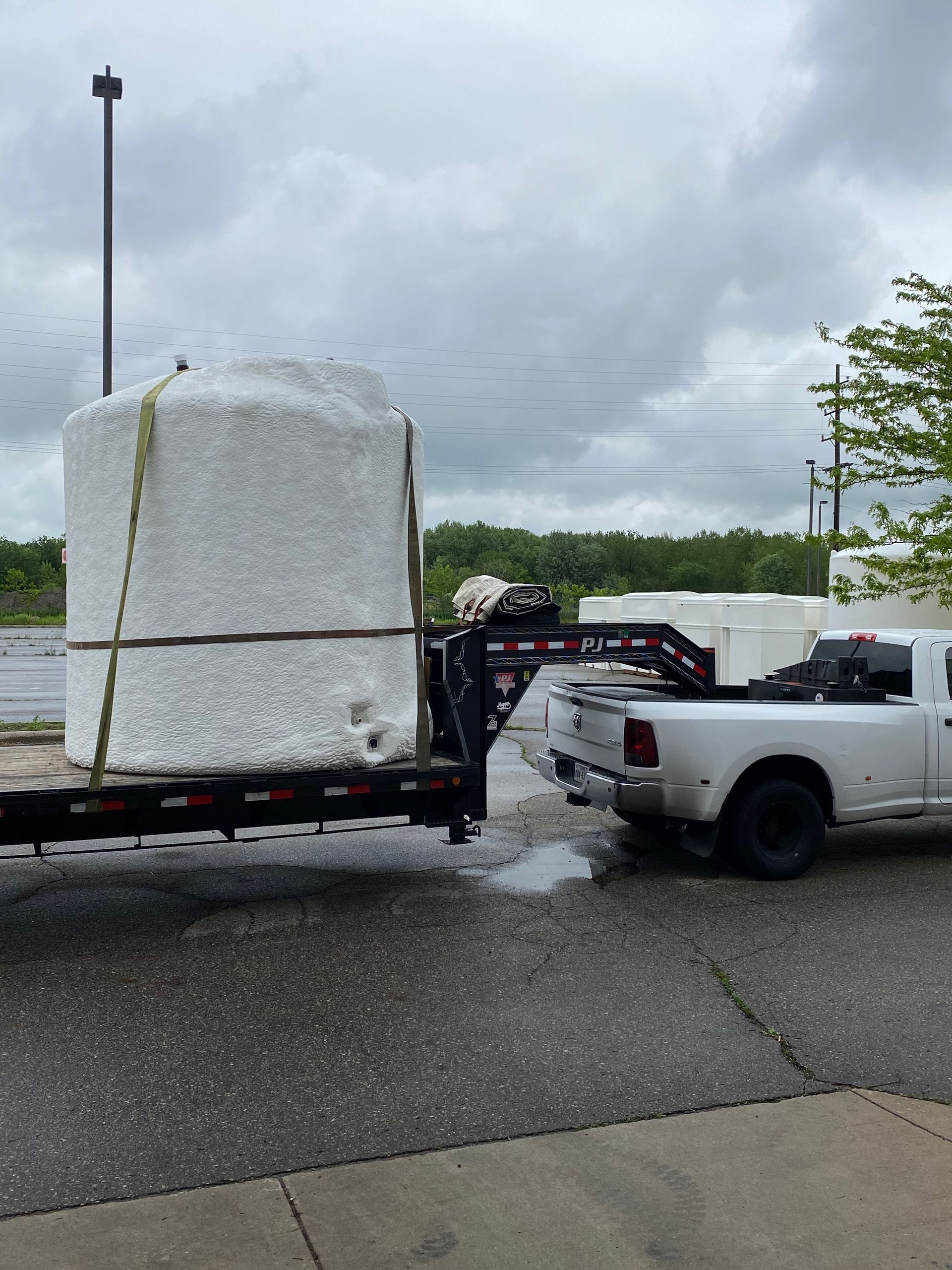 White truck towing a large, white cylindrical object on a trailer under a cloudy sky.