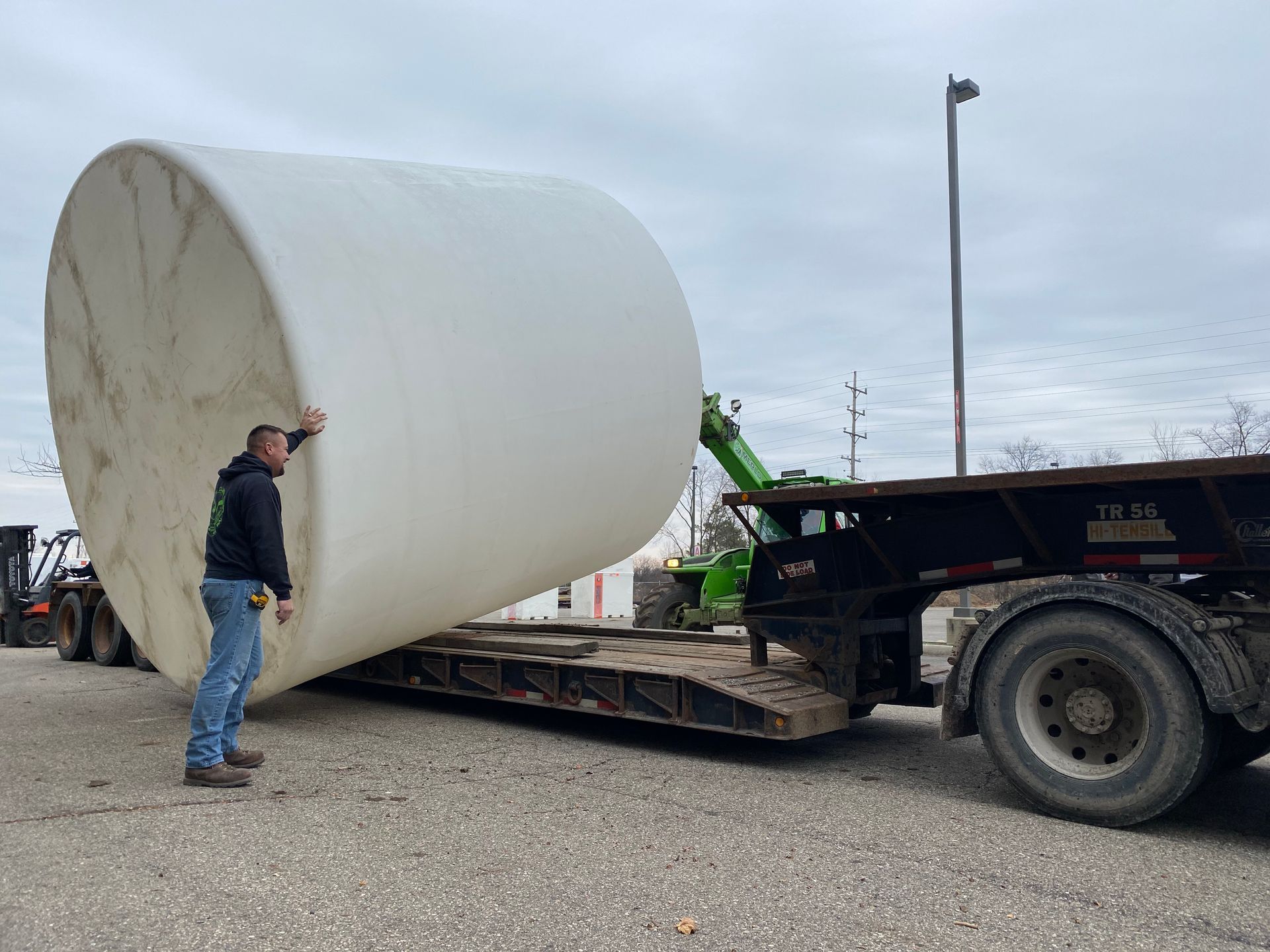 Man and forklift maneuvering large white tank onto a flatbed trailer.