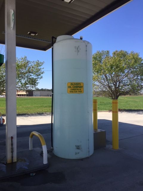 White tank for oil containment at a gas station, yellow sign on it, sunny day.