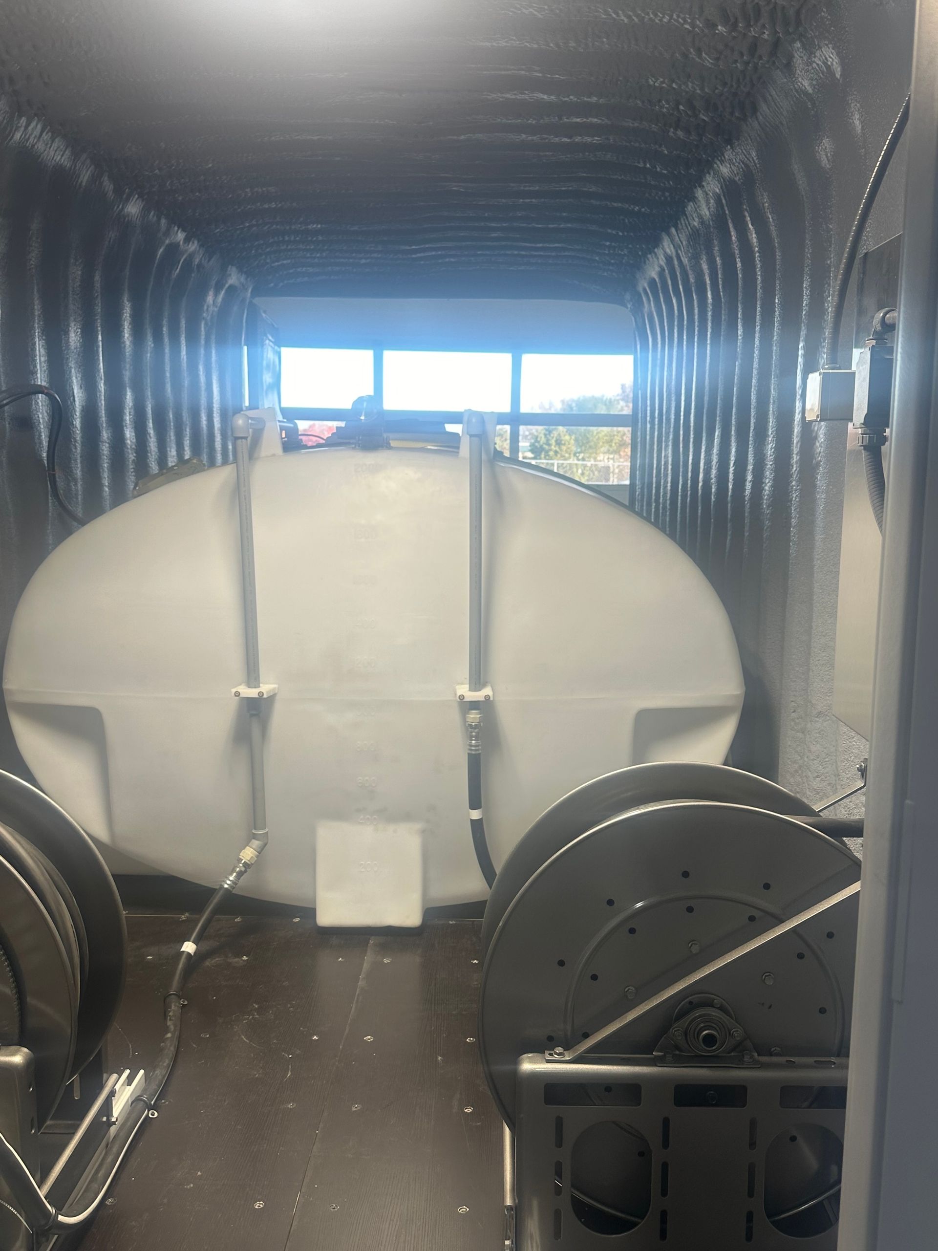 Large white tank inside a metal-walled container, two reels are in the foreground, and a window is visible in the distance.