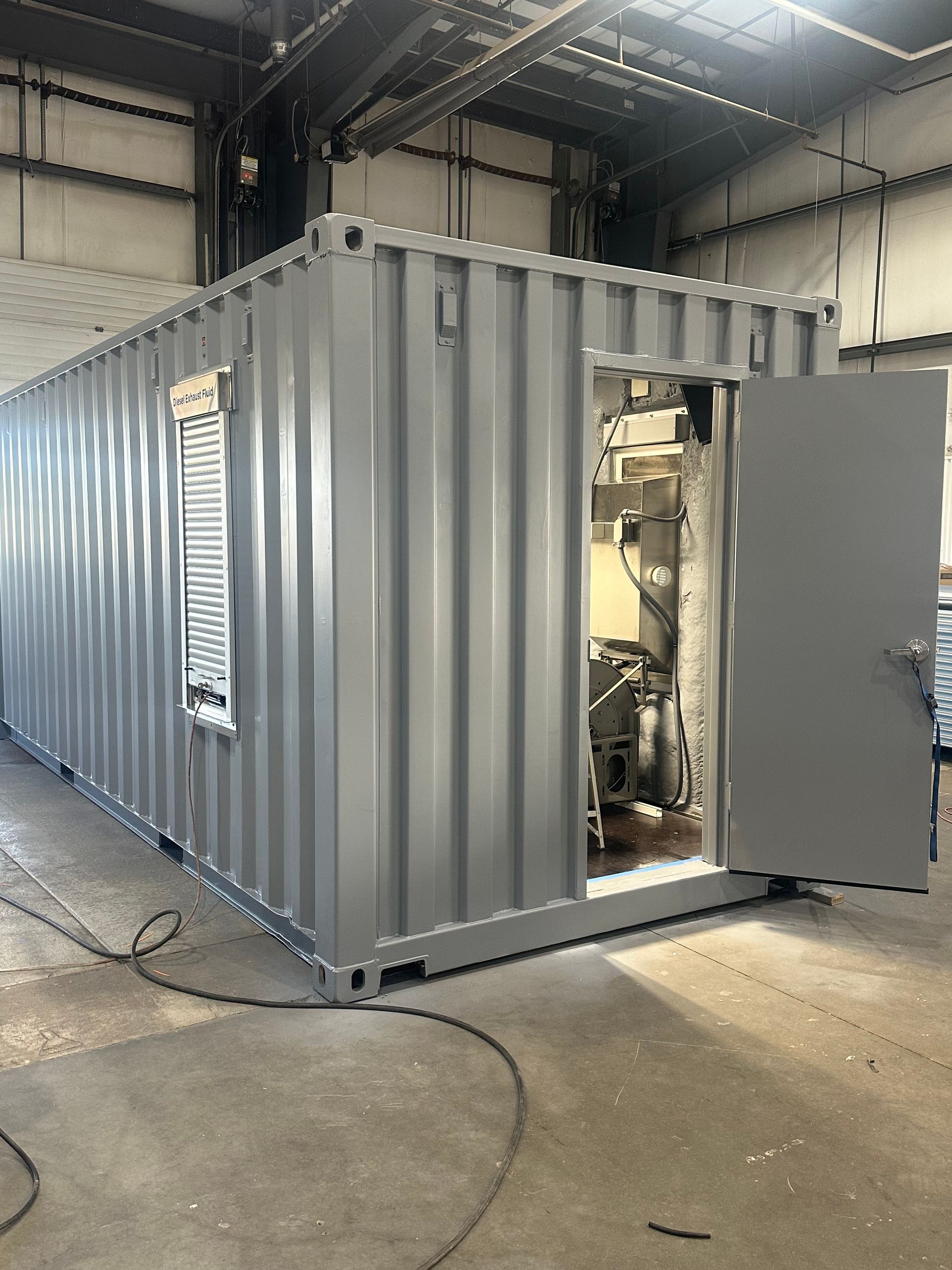 Gray shipping container modified with a door and window, placed indoors.