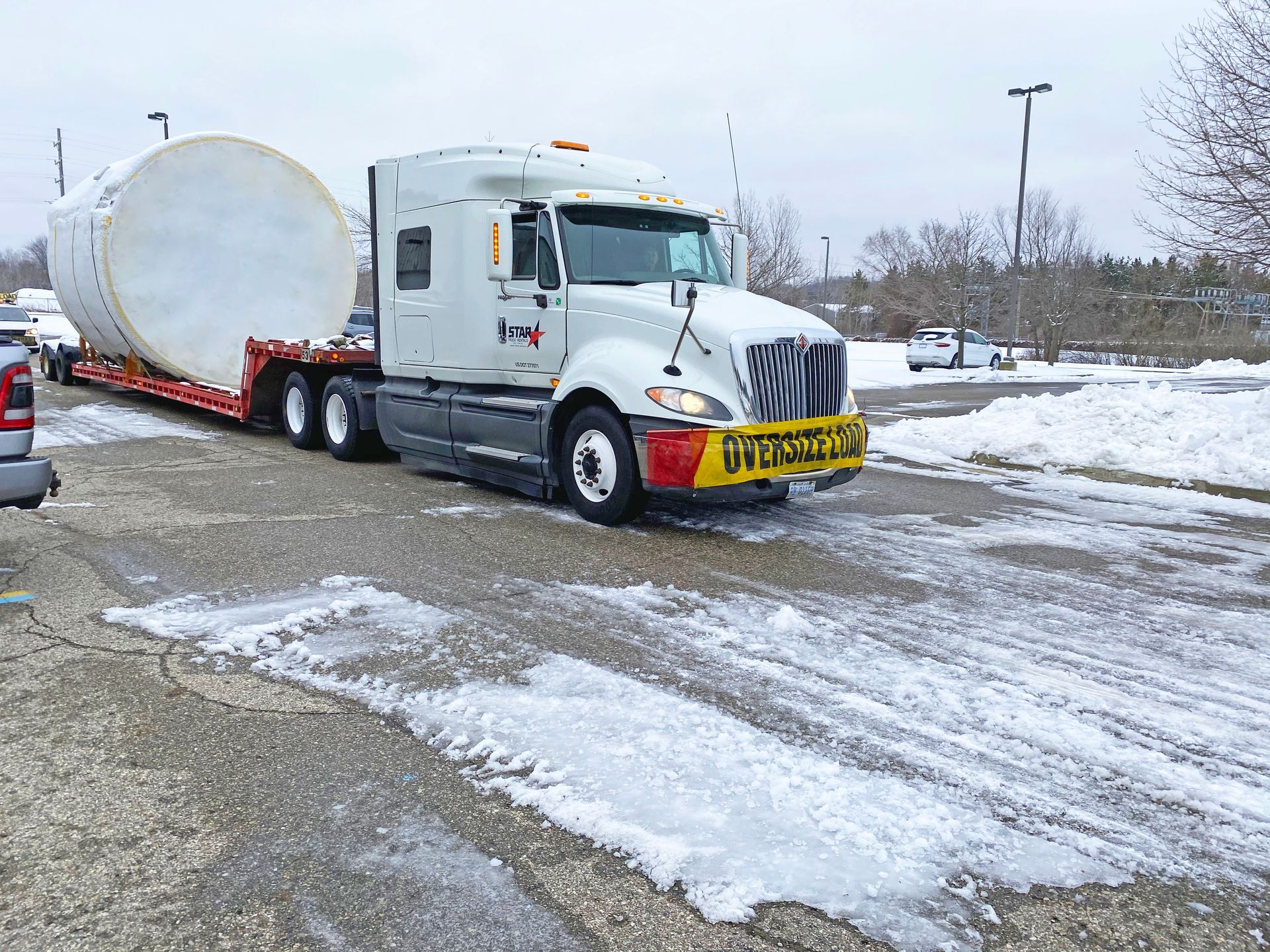 Semi-truck hauling an oversized, white cylindrical object on snowy, icy pavement. 
