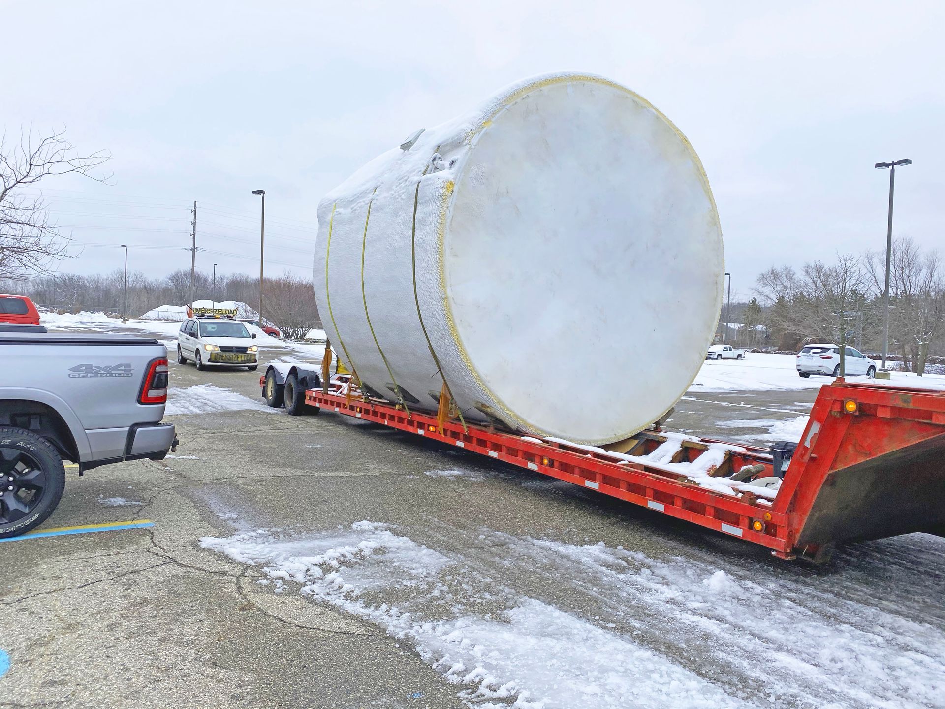 Large cylindrical tank on a flatbed trailer, pulled by a truck in a snowy parking lot.