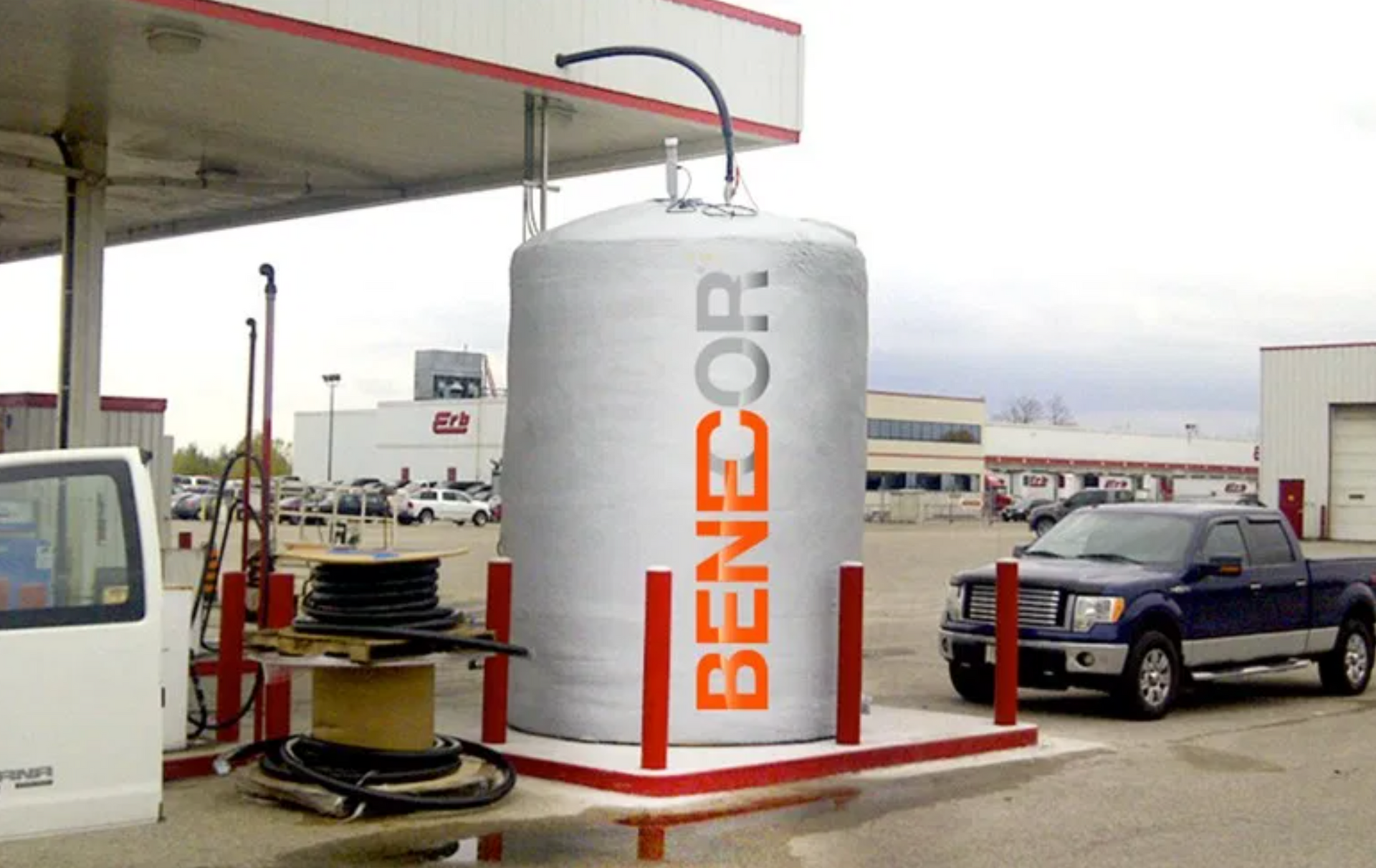 Large BENCOR propane tank at a gas station next to a pickup truck, gray and orange text.