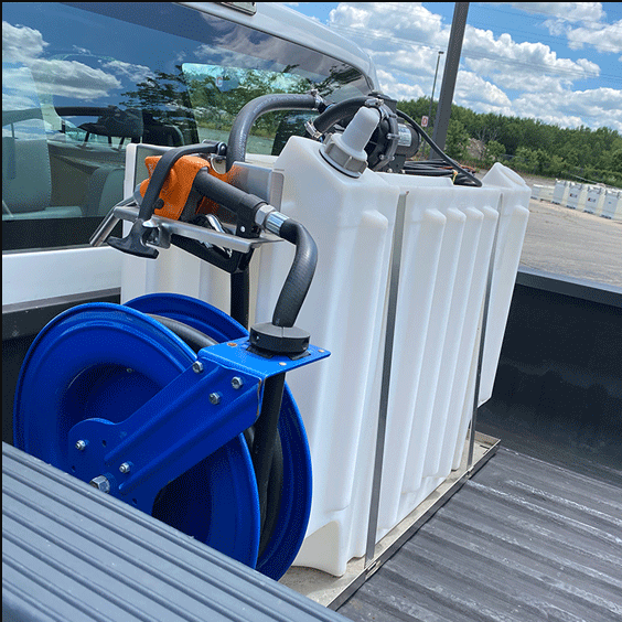 Fuel tank with nozzle and blue hose reel in the bed of a white truck on a sunny day.