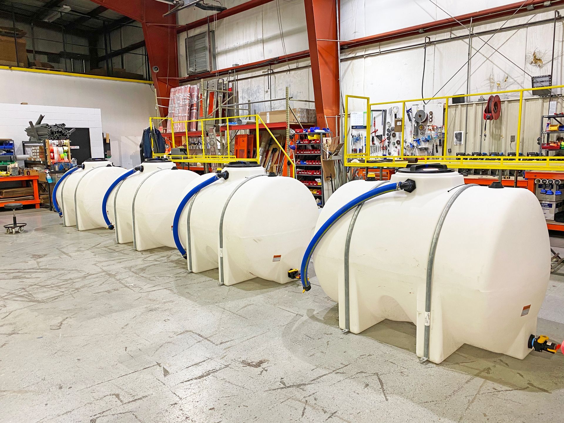 Row of white industrial tanks with blue tubing in a warehouse.