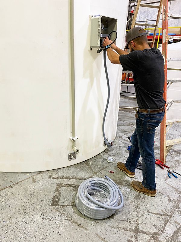 Man in jeans wiring electrical box on a white curved wall, a coil of cable on the floor.