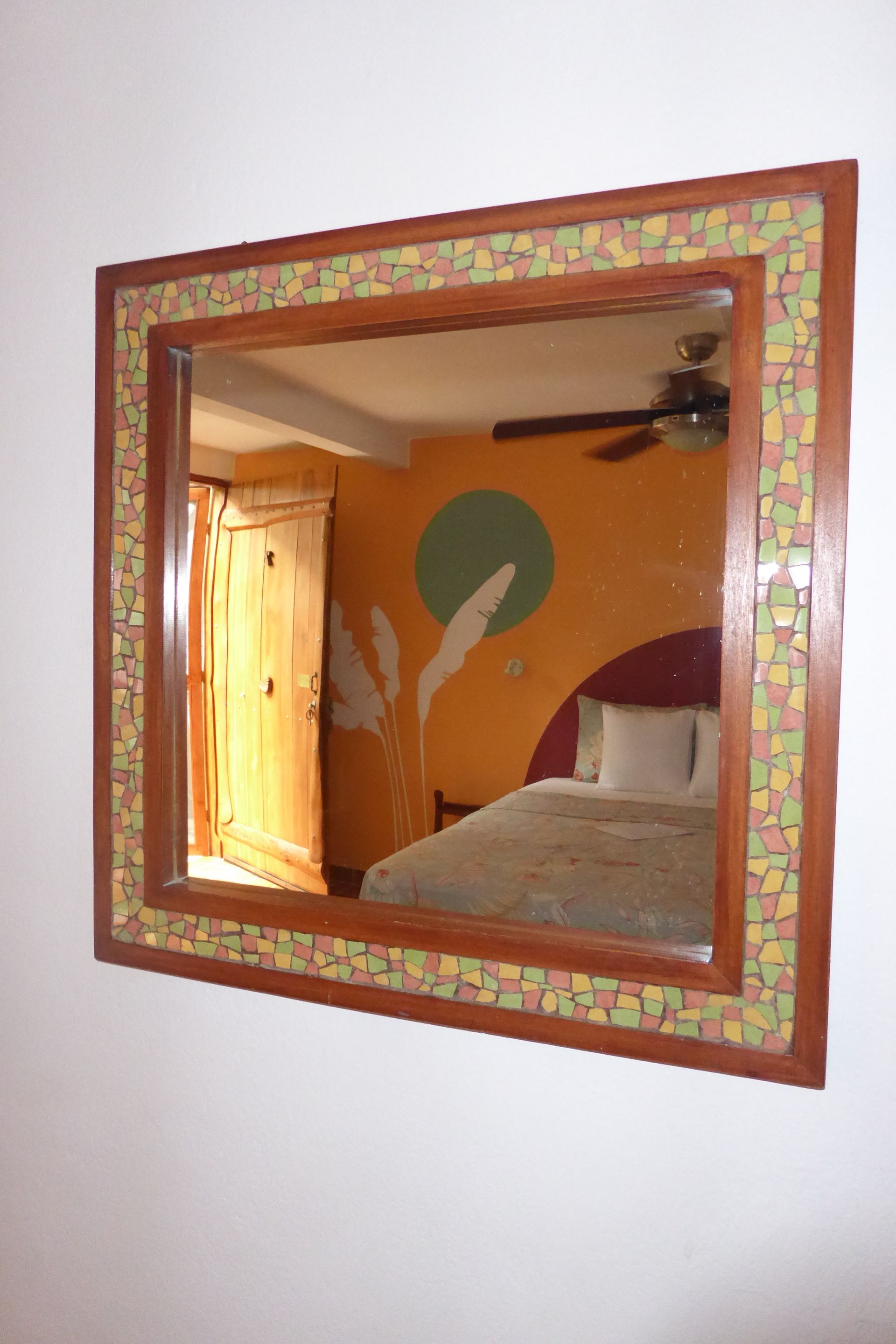 A mirror shows a bedroom with a bed and a ceiling fan